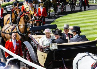 Royal Ascot Race Meeting at the prestigious Ascot racecourse in Berkshire. Royal Procession. Arrival of members of the Royal Family. Queen Elizabeth II and Prince Philip sitting in a horse-drawn carriage with two men. Accompanied by men wearing military uniform walking and on horse-back. Credit: Visit Britain